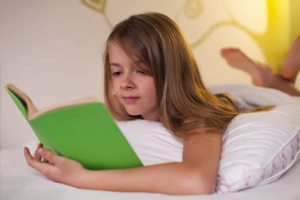 istock Young girl lying on her belly in bed - reading a book, shallow depth 1198627128