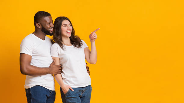 istock Happy interracial spouses cuddling and pointing aside at copy space 1198633299