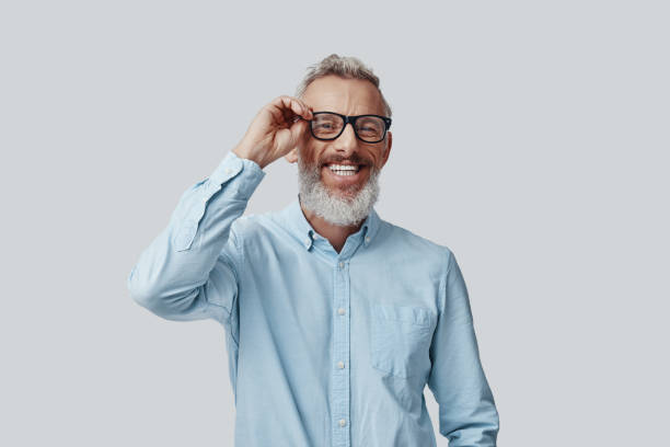 istock Happy mature man looking at camera and adjusting eyewear while standing against grey background 1198634635