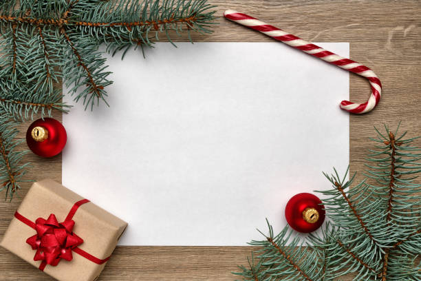 istock Christmas or New Year composition. White sheet of paper with copy space, gift box, candy cane, Christmas ball and Christmas tree branches on wooden background. Flat lay, view from above 1198637301