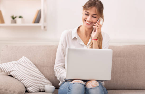 istock Woman Talking On Phone Working On Laptop Sitting On Couch 1198639940