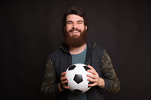 Portrait of cheerful young man holding soccer ball and looking at the camera