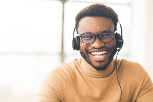 Happy consultant with headset looking at camera Helpline Concept. Head shot of smiling black man wearing headset at office looking at camera. Empty space cross section stock pictures, royalty-free photos & images