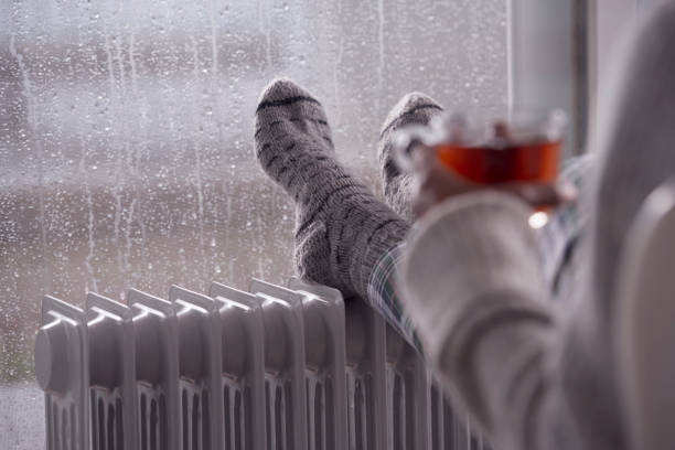 Close up heating female feet with woolen socks on the radiator heater. The woman drinking hot tea. stock photo