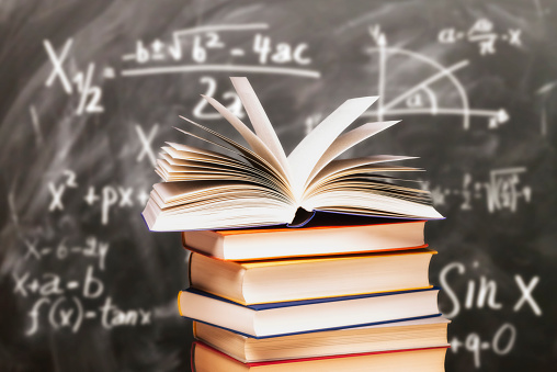 An orange cup on a stack of books on a dark library background. Book background. Education, learning and reading concept. Copy space.