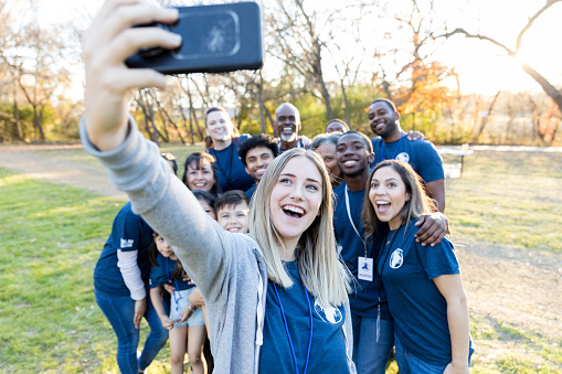Happy young woman takes a selfie with a group of neighbors, who have successfully cleaned up their community park.
