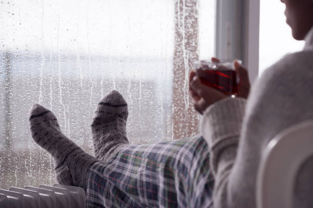 Over the shoulder image of a woman drinking tea at home in cold and wet weather. stock photo