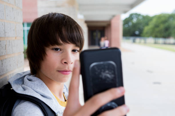istock Young boy standing alone outside school takes selfie with phone 1198645813