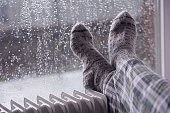 Woman's feet wearing gray woolen socks, warming cold feet on oil heater in the rainfall winter season.