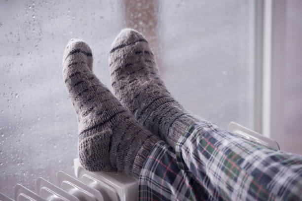 ноги женщины носить серые шерстяные носки, потепление холодные ноги на масляный обогреватель в зимний сезон осадков. - window rain winter house стоковые фото и изображения