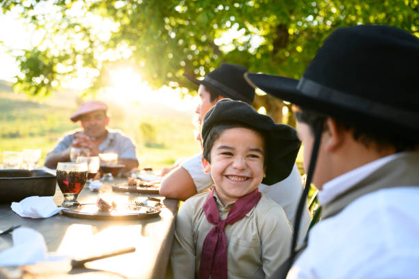 Argentine gaucho brothers 5 and 10 years old sitting side by side and smiling at each other during outdoor midday meal.