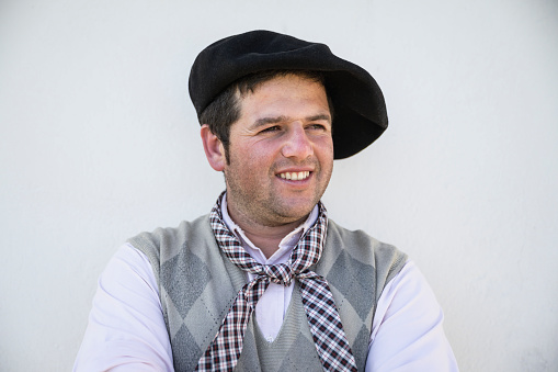 Close-up of relaxed gaucho in early 30s wearing traditional boina headwear, plaid scarf, and open collar shirt with argyle waistcoat looking away from camera.