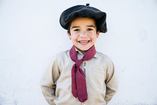 Close-up of Argentine boy gaucho wearing traditional boina headwear, scarf, open collar shirt, and smiling at camera.