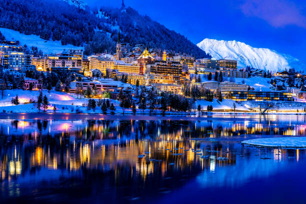 blick auf schöne nachtlichter von st. moritz in der schweiz bei nacht, mit reflexion vom see und schneebergen im hintergrund - st moritz fotos stock-fotos und bilder