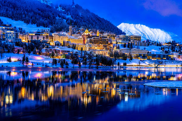 View of beautiful night lights of St. Moritz in Switzerland at night, with reflection from the lake and snow mountains in backgrouind View of beautiful night lights of St. Moritz in Switzerland at night, with reflection from the lake and snow mountains in backgrouind engadine stock pictures, royalty-free photos & images