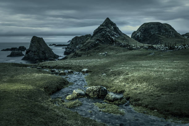 a stream running into the sea along wild rugged craggy irish coastline at Ballintoy, Northern Ireland, a tourist attraction and where scenes from Game of Thrones were filmed, in early winter morning under dark cloudy moody sky and some light painting
