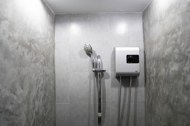 Instant tankless electric water heater installed on grey tile wall with input and output pipe outlet and elcb safety breaker system and silver shower. stock photo