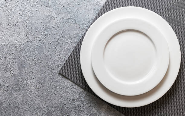 istock Empty white plate served on relief napkin and embossed gray concrete background. Top view mock up for menu 1198660684