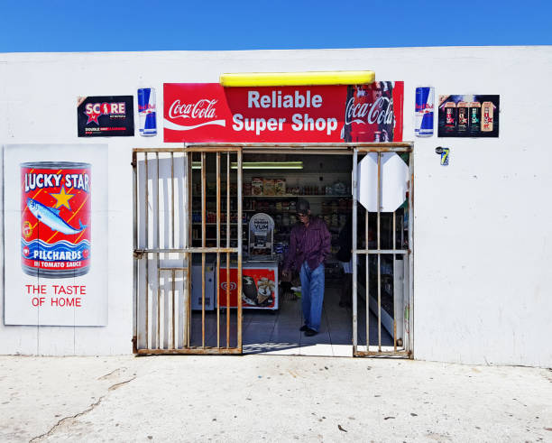 Customer leaving tiny Cape Town convenience store Cape Town, South Africa - December 16, 2019: A shopper leaves a small convenience store in the lower-middle-class suburb of Grassy Park. Such shops, typically operated by recent immigrants from the Indian subcontinent or countries further north in Africa, have mushroomed across South Africa in recent decades. red bull mini stock pictures, royalty-free photos & images