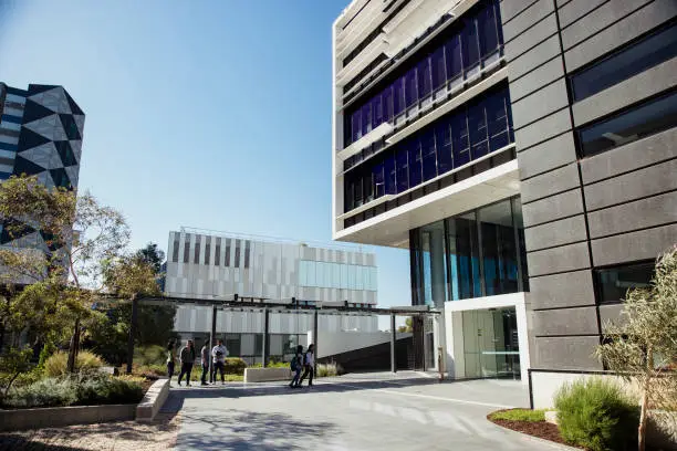 A wide-view shot of a group of university students walking to their class on campus, it's a sunny day in Australia.