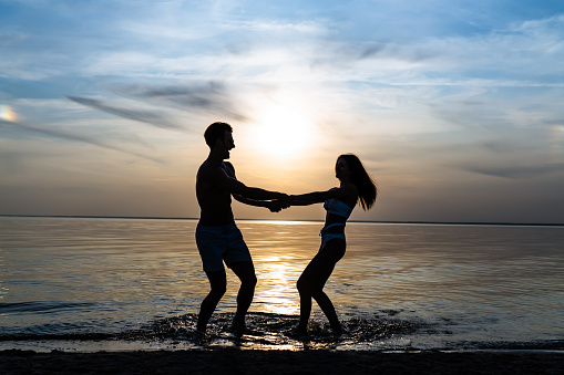 The man and woman spinning in water against the beautiful sunset