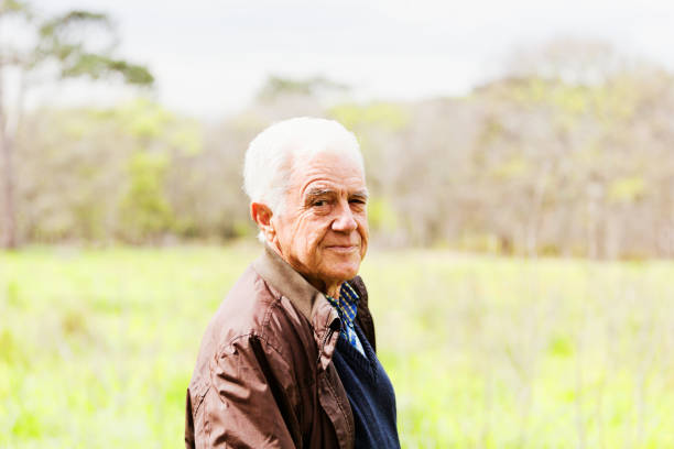 A contented looking senior man walking in the countryside turns to camera and smiles.