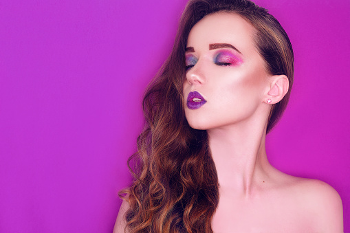 Fashion model with creative pink and blue make up.  Beauty art portrait of beautiful girl with colorful abstract makeup. Beautiful Eyes Glitter . Nude bright lips, long cerly hair. Pink background