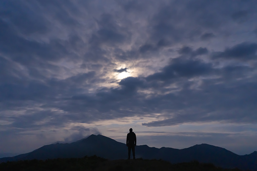 The man standing on a mountain on the cloud sky background