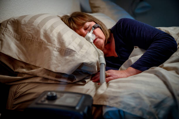 mulher envelhecida média em seus anos 50 que dormem pacificamente em sua cama usando uma máquina de cpap para fornecer a terapia para o apnea de sono - sensor de pressão - fotografias e filmes do acervo