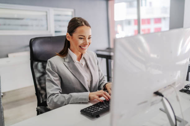 istock Young hardworking smiling Caucasian businesswoman sitting in her office and using computer. Corporate business concept, 1198692096
