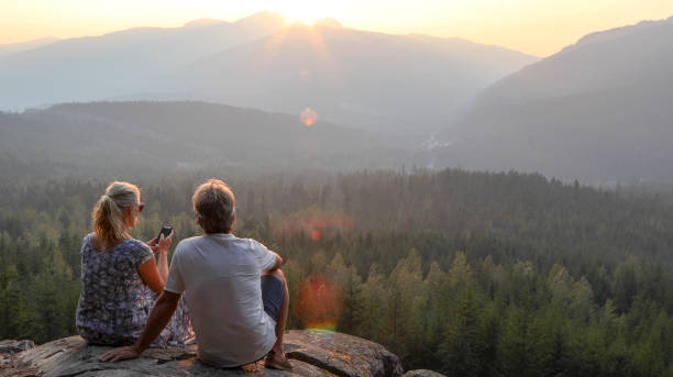 istock Mature couple relax on mountain ledge, look out to view 1198692244