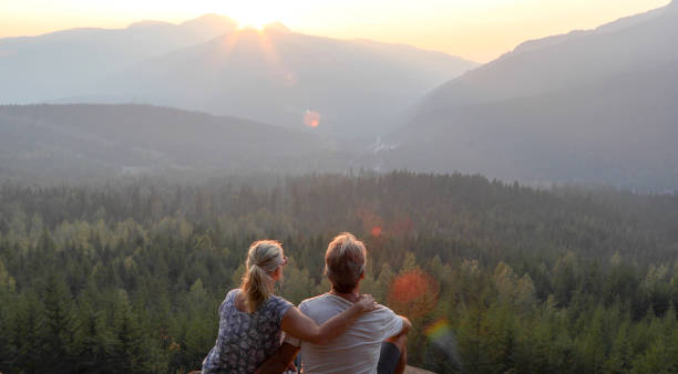 Mature couple relax on mountain ledge, look out to view