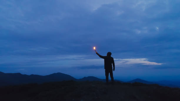Photo of The man with a firework stick standing on the evening mountain