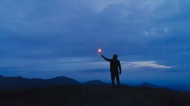 Photo of The man with a firework stick standing on the evening mountain
