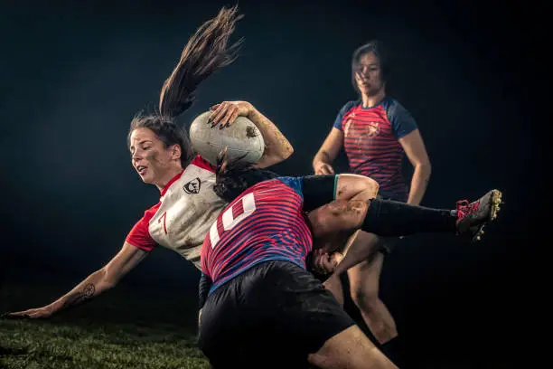 Female rugby player getting tackled against a black background.
