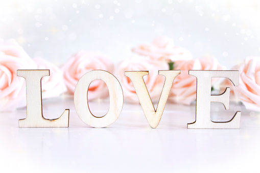 The word Love with pale pink roses in the background, bokeh lighting and copyspace.