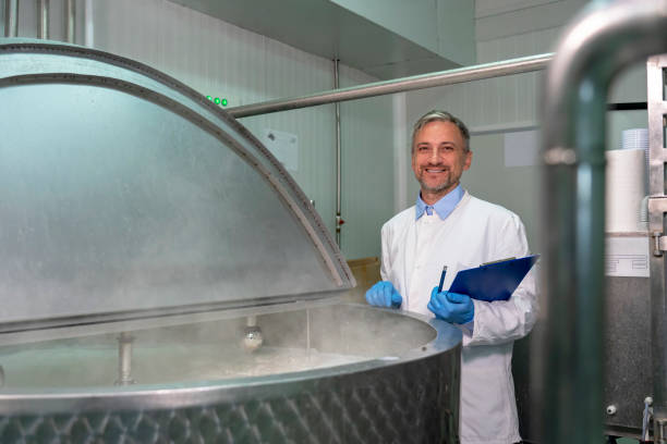 istock Smiling Dairy Plant Food Engineer Standing Beside Stainless Steel Milk Pasteurizer Tank 1198697407