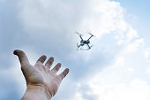 The man's hand reaches for the flying drone. The drone is out of focus.