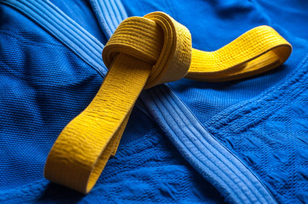 Yellow judo, aikido, or karate belt, tied in a knot Yellow judo belt tied in a knot layng on blue judogi yellow belt stock pictures, royalty-free photos & images