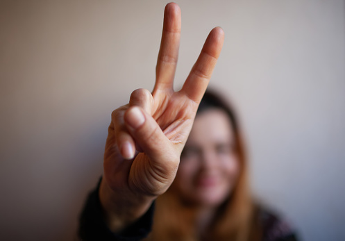 Young woman shows her victory sign with her fingers out of focus, on a light background