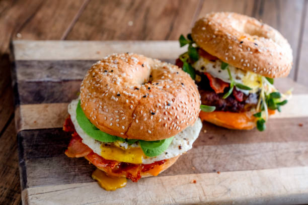 istock Breakfast Bagel with Egg, Greens, Avocado, Bacon, Sausage and Cheese on a Rustic Cutting Board 1198713490