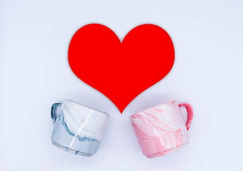 Flatlay composition. Two marble cups in pink and gray and red heart on a white background. Valentines day concept.