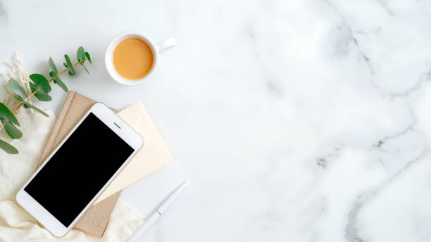 istock Home office desk table with smartphone screen mockup, paper notepad, cup of coffee, eucalyptus leaf on marble background. Elegant feminine workspace with stylish accessories. Flat lay, top view. 1198721003