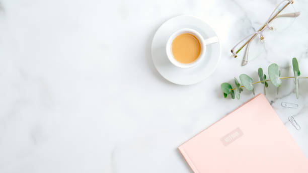 istock Cozy home office desk table with pink paper notebook, glasses, eucalyptus leaf, coffee cup on marble background. Top view, flat lay, copy space. Elegant feminine workspace with stylish accessories 1198721008