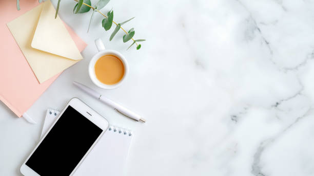 istock Flat lay home office desk. Women workspace with paper notebook, coffee cup, envelope, smartphone on marble table. Top view feminine background with copy space. 1198721011