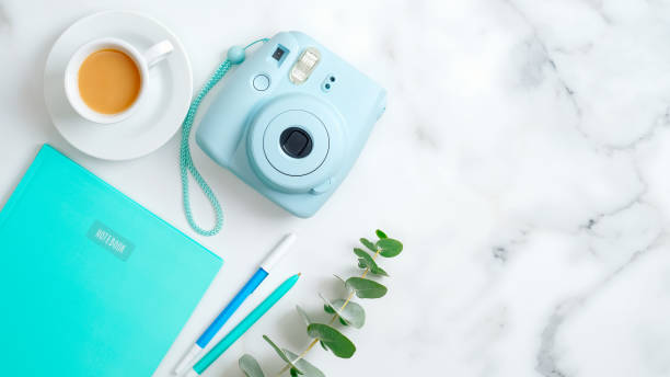 istock Feminine workspace with modern instant camera, coffee cup, mint notepad, stationery and eucalyptus leaf on marble table. Flat lay, top view, copy space. Freelancer home office desk concept. 1198721029