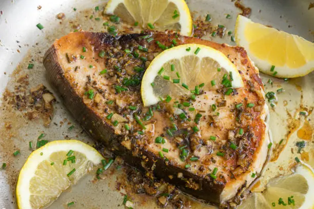 A pan-fried swordfish steak garnished with lemon wedges and chives