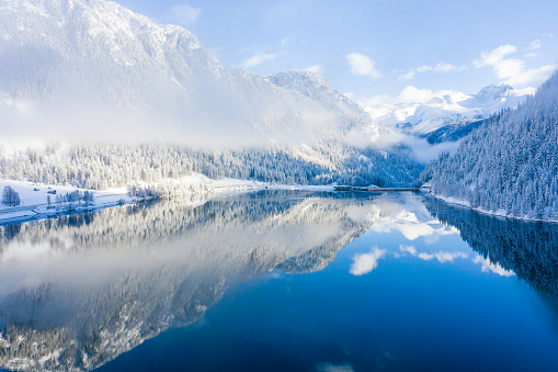 Beautiful winter lake with a reflection of the Swiss mountains in Switzerland. Magical winter forest covered in snow, surrounded by mountains with a lake in the valley. Epic scenery.