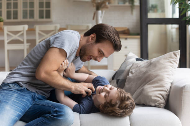 istock Father tickles lovable son having fun in living room 1198734199