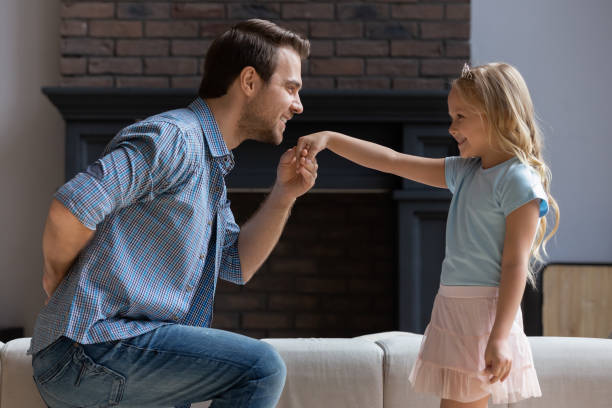 Father making curtsey took hand of daughter for a kiss Side view dad standing one bended knee making curtsey in front of kid girl took her hand for kiss, concept of gentlemen gesture, deep devotion and connection and endearment between father and daughter curtseying stock pictures, royalty-free photos & images